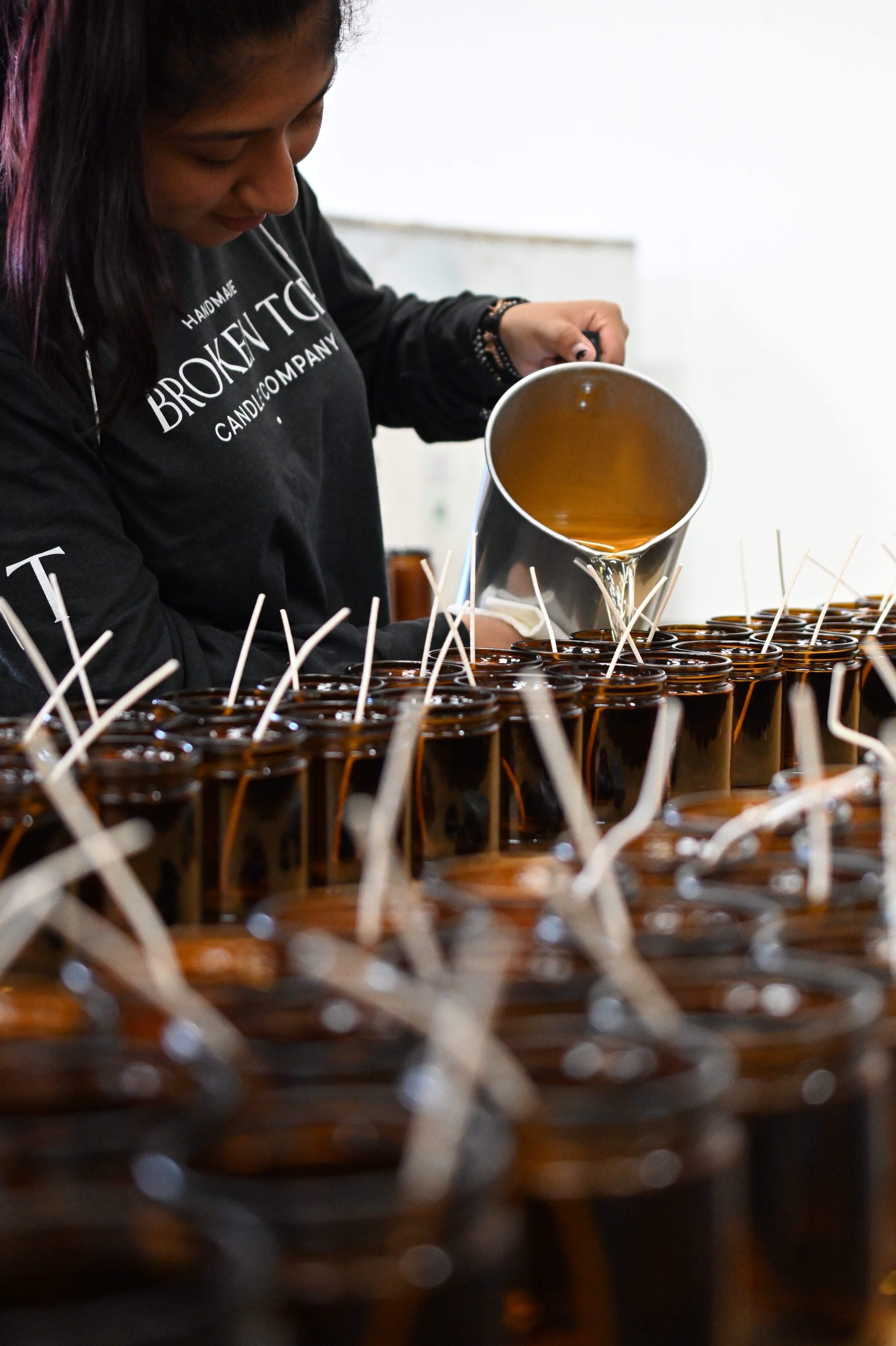 Hot wax being poured by hand into glass candle vessels. 