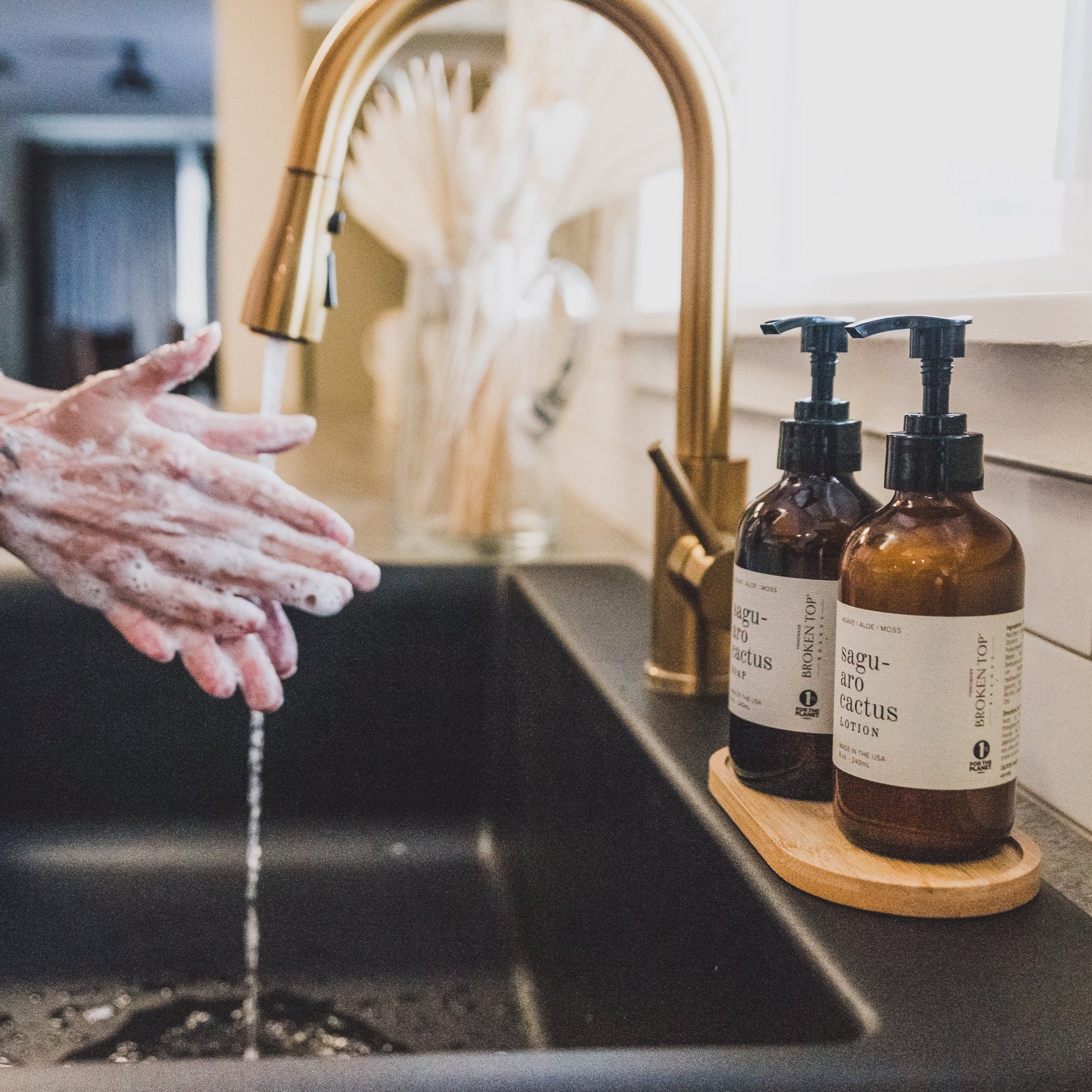 8oz Saguaro Cactus Liquid Soap and 8oz Saguaro Cactus Body Lotion next to a kitchen sink with hands washing. 