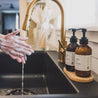 8oz Saguaro Cactus Liquid Soap and 8oz Saguaro Cactus Body Lotion next to a kitchen sink with hands washing. 