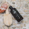 16oz Santal Noir Body Wash next to a luffa on stone shower floor. 