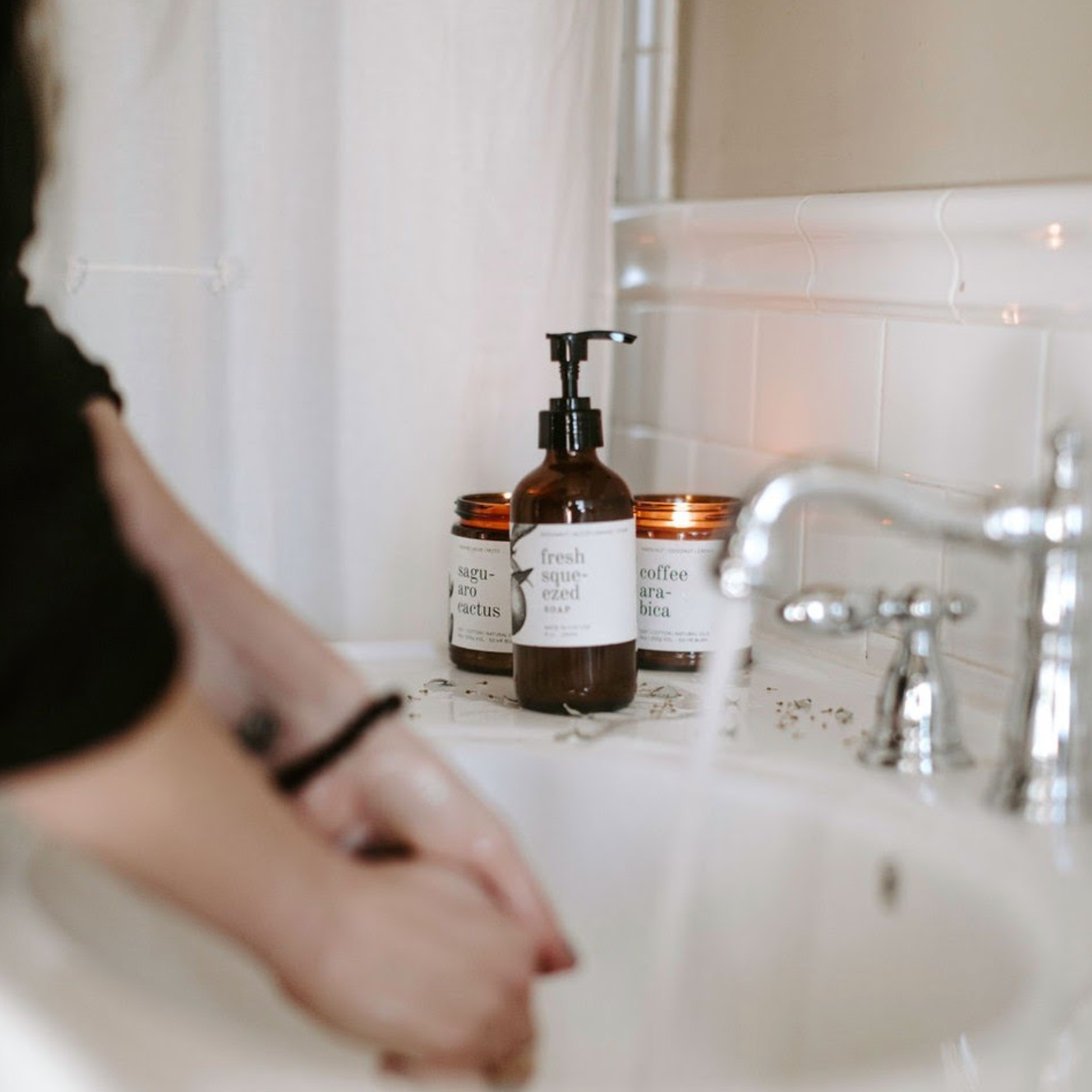 8oz Fresh Squeezed Liquid Soap on a bathroom countertop in front of 2 soy candles. 