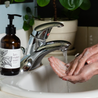 8oz Lavender Mint Liquid Soap next to a bathroom sink with hands washing. 