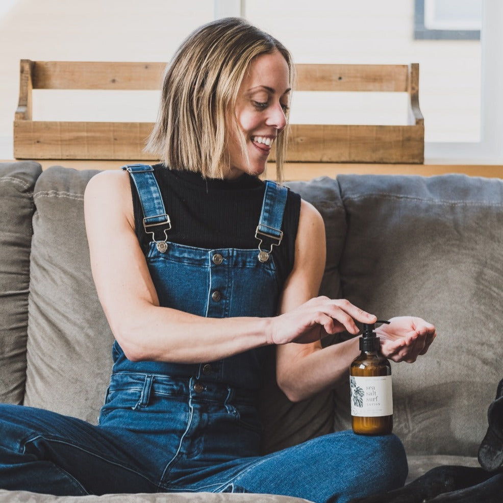 8oz Sea Salt Surf Body Lotion being used by a woman sitting on a couch. 