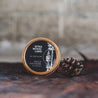 Sitka Woodland Solid Cologne next to a small pine cone. 