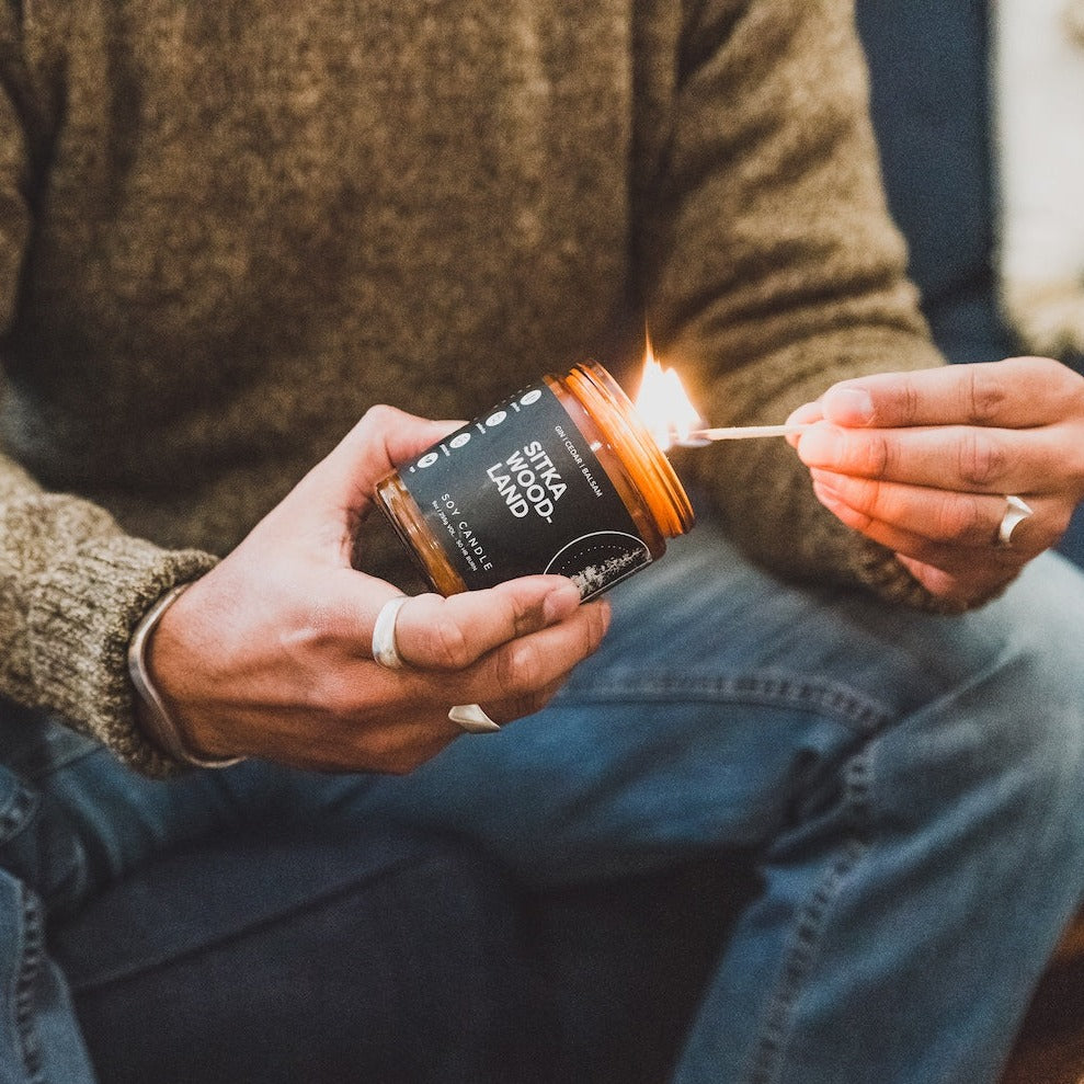 9oz Sitka Woodland Soy Candle being lit by a match. 