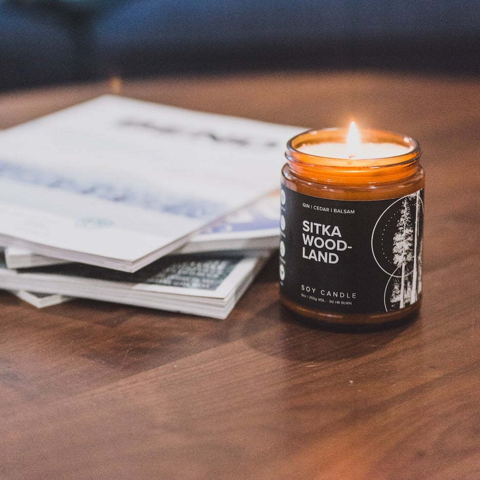 9oz Sitka Woodland Soy Candle on a coffee table next to a stack of magazines. 