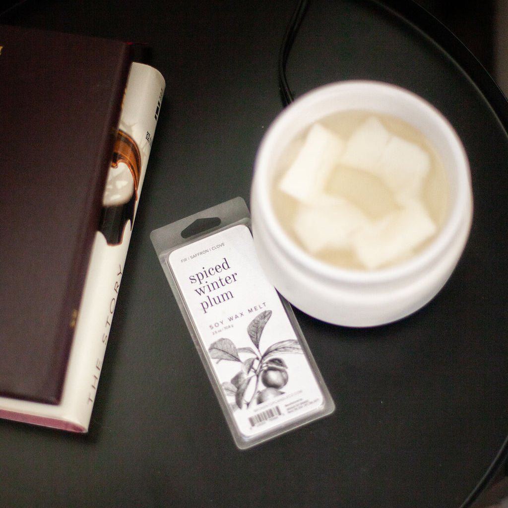 Spiced Winter Plum Soy Wax Melt on black side table next to a white wax melter and stack of books. 