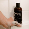 16oz Tobacco Teak Body Wash in a shower being held by a hand. 