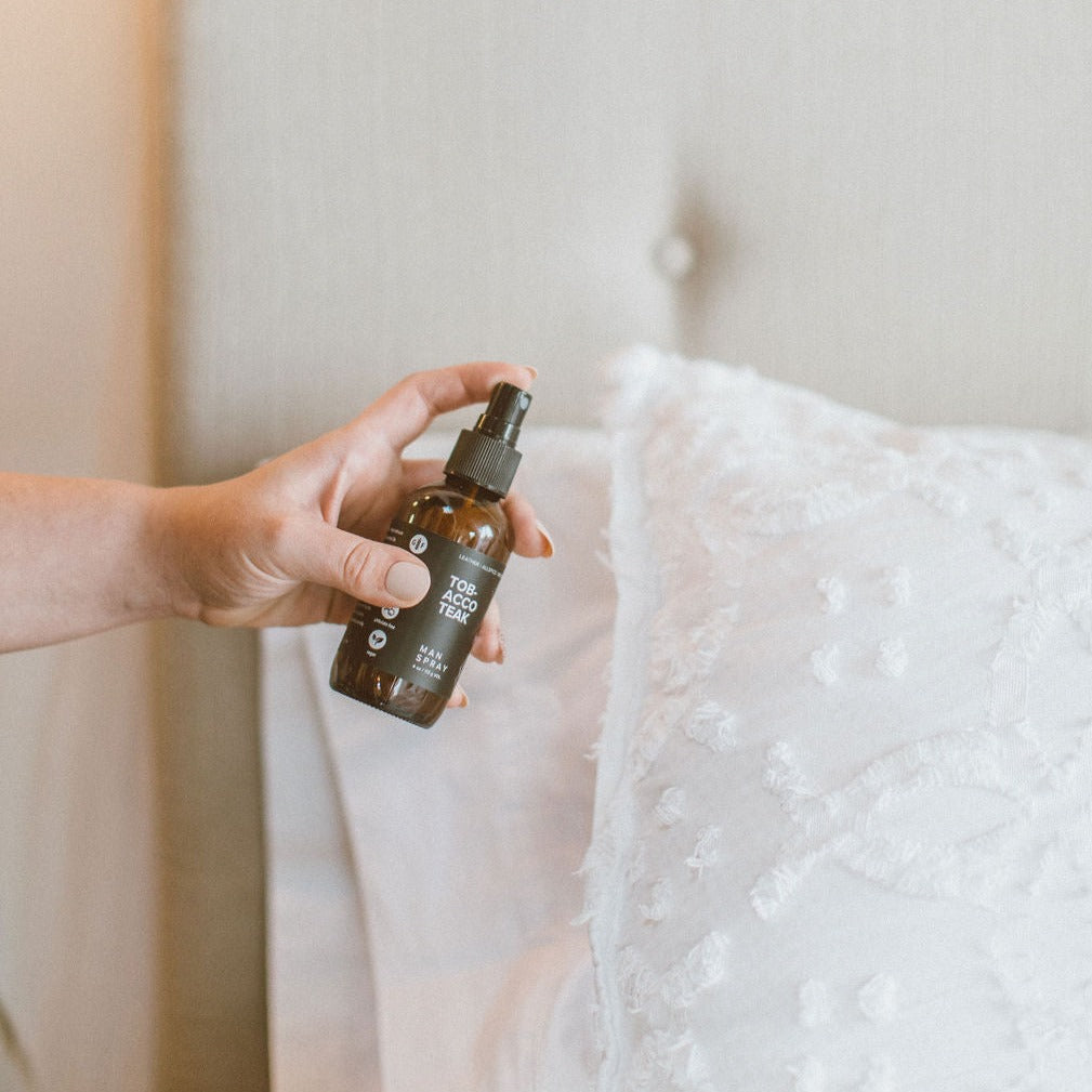 4oz Tobacco Teak Man Spray being sprayed onto pillows by a hand. 