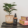 4oz Tobacco Teak Man Spray next to two books and a small plant. 