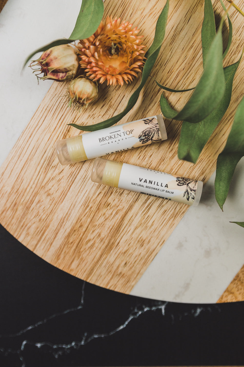 Two Vanilla Lip Balms next to decorative dried plants. 