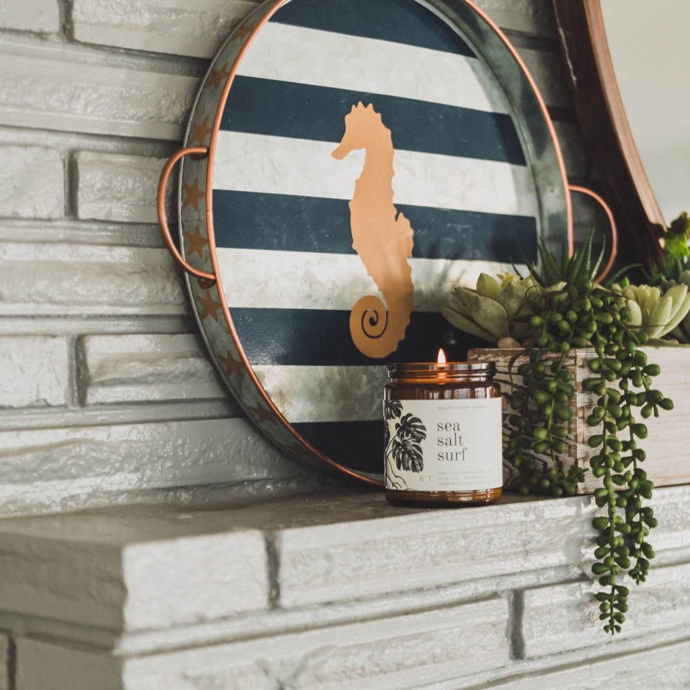 9oz Sea Salt Surf Soy Candle on a mantle next to small decorative plants. 