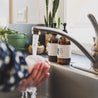 8oz Sea Salt Surf Liquid Soap and 8oz Sea Salt Surf Body Lotion next to a kitchen sink with hands washing. 