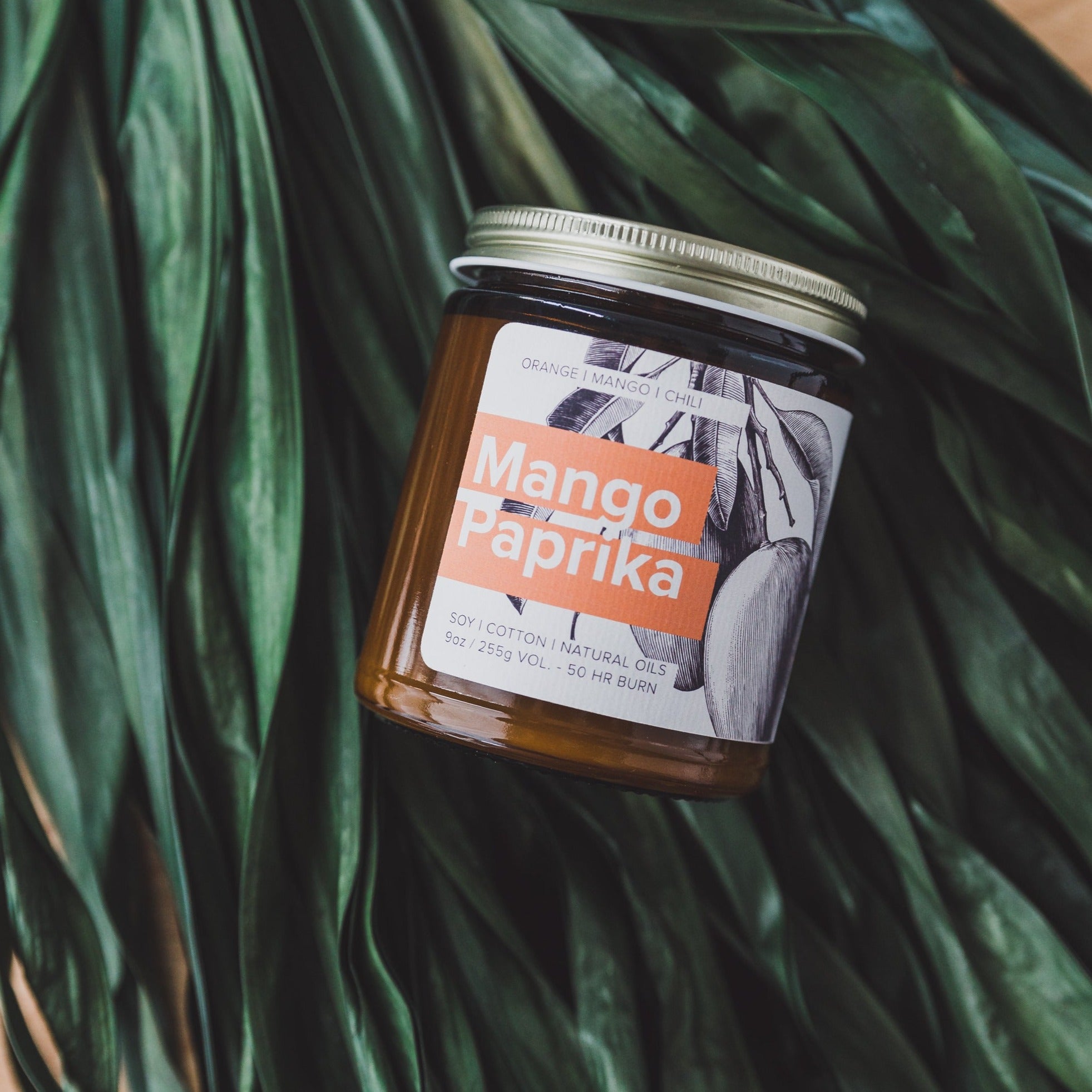 9oz Mango Paprika Soy Candle on leafy green background. 