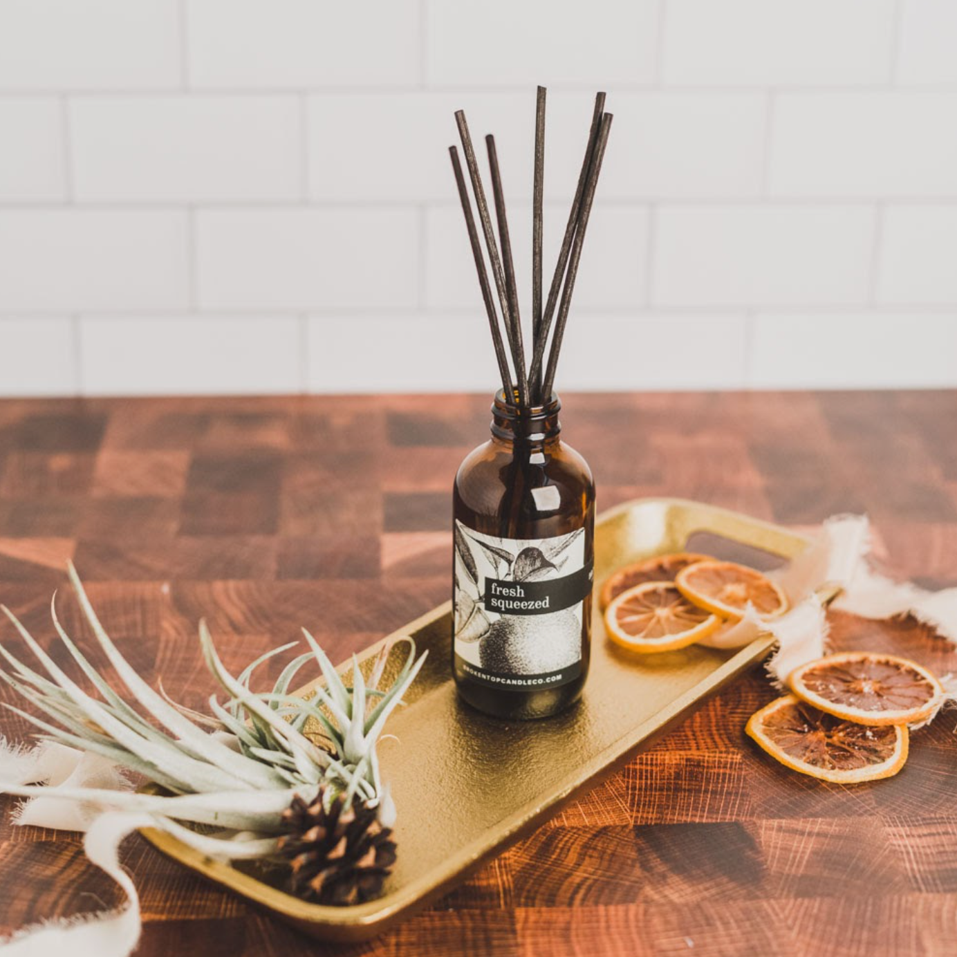 Fresh Squeezed Reed Diffuser on a gold tray next to decorative orange slices. 