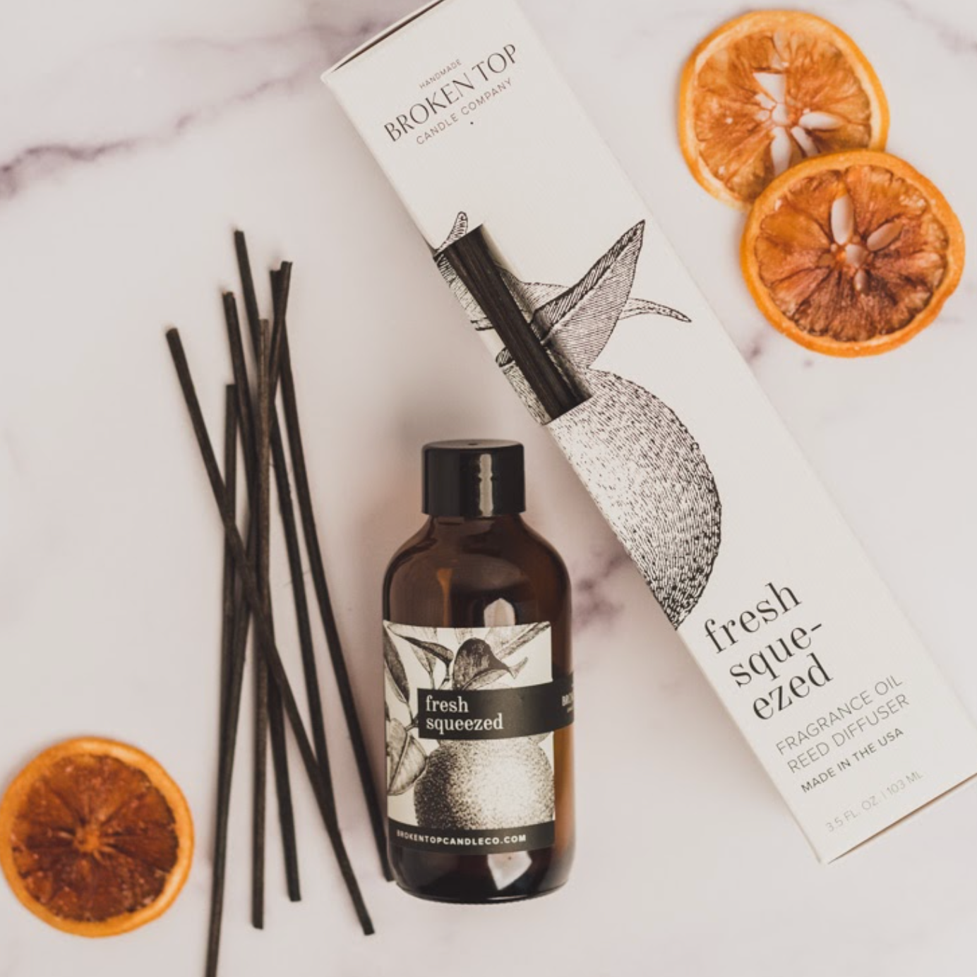 Fresh Squeezed Reed Diffuser on marble countertop next to decorative orange slices. 