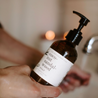 8oz Coconut Sandalwood Liquid Soap being held in front of a sink. 