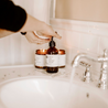 8oz Coconut Sandalwood Liquid Soap being dispensed next to a bathroom sink. 