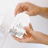 Lavender Mint Bar Soap being unwrapped by two hands. 