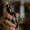 4oz Tobacco Teak Man Spray being sprayed by a hand. 